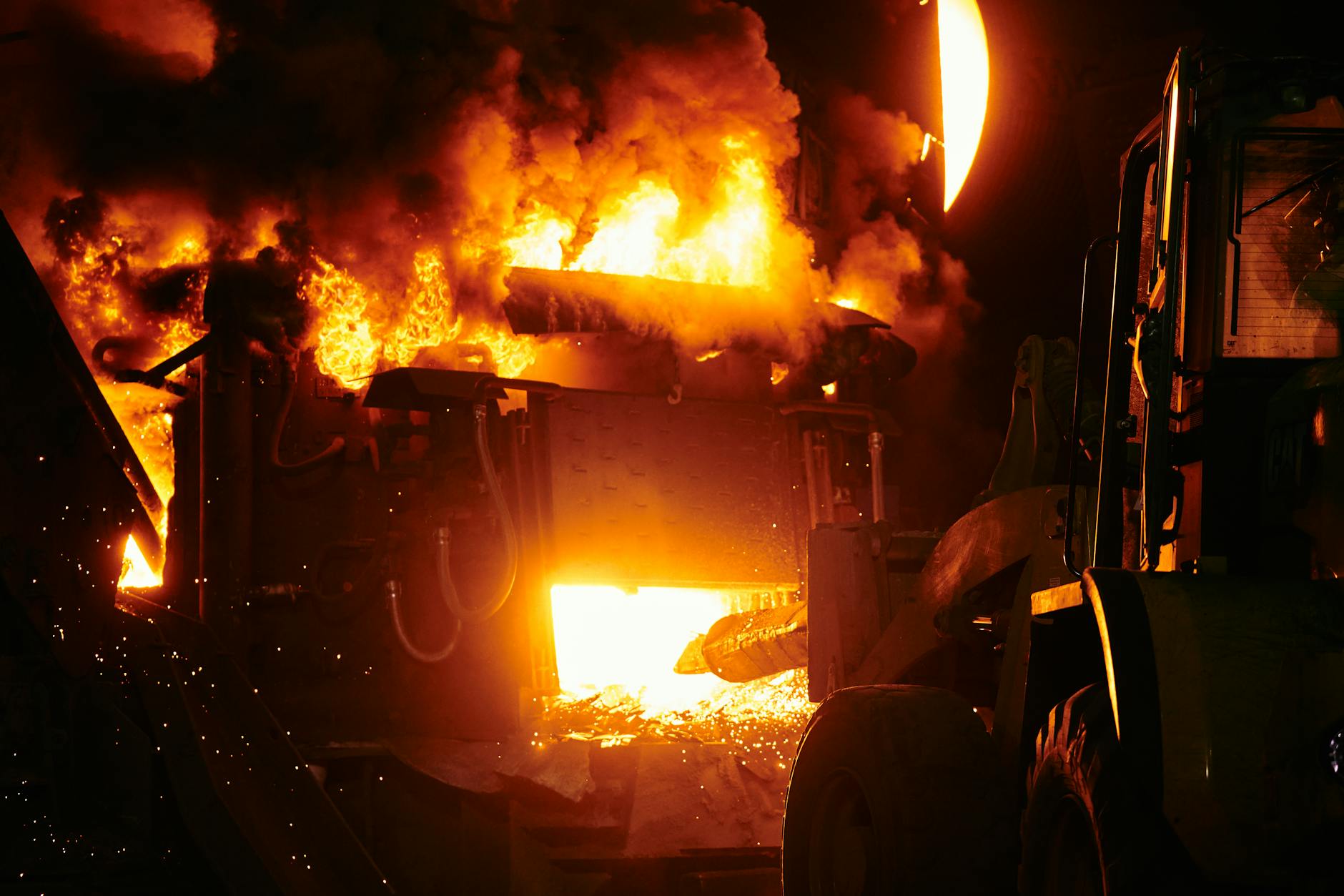 Dramatic image of an industrial furnace with bright flames and heavy machinery at night.