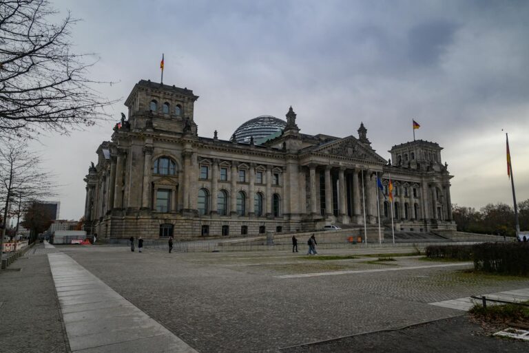 View of the iconic Reichstag building in Berlin under a cloudy sky, featuring its distinctive glass dome.
